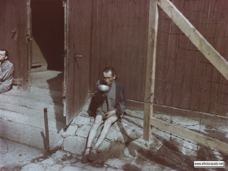 Un sobreviviente demacrado bebe de un recipiente de metal frente a un barracón en Buchenwald.